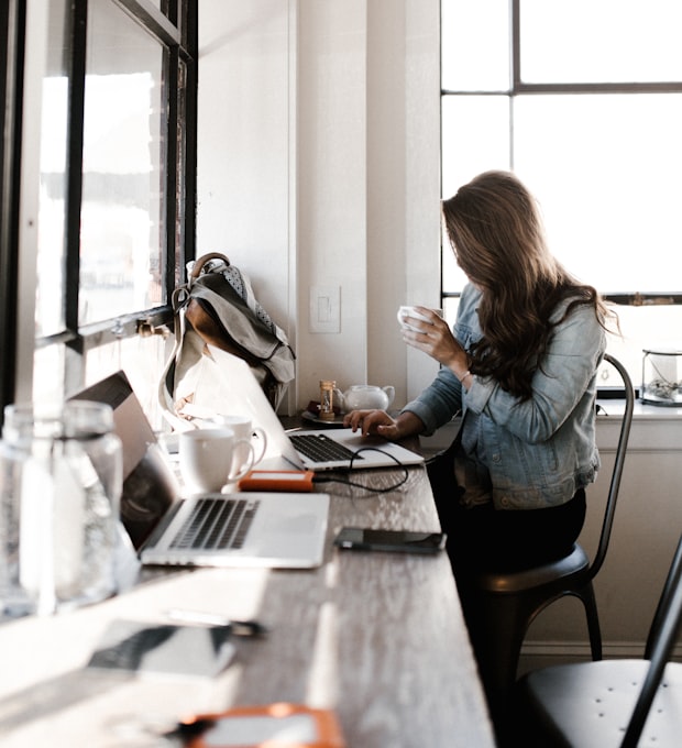 Person mit Kaffeetasse am Laptop an einer Fensterbank